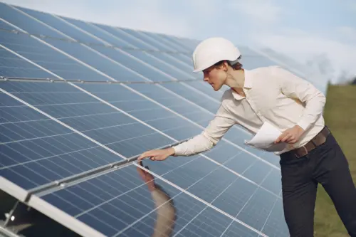 A businessman in a white hard hat stands among rows of solar panels