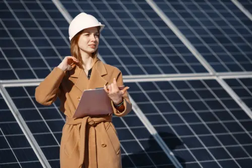 businesswomen work at a solar power plant, checking equipment with a tablet and a checklist.