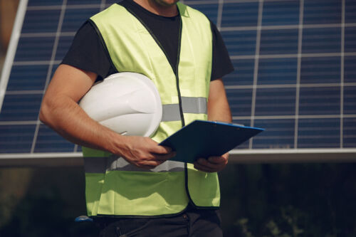 Man with a white helmet standing near a solar panel.