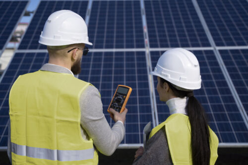 Close-up of two workers examining individual solar panels within a sprawling solar power plant.