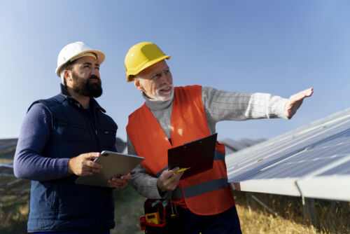 Two technicians inspect photovoltaic solar panels in a field.