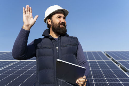 A solar technician stands proudly in front of a newly installed solar panel array.