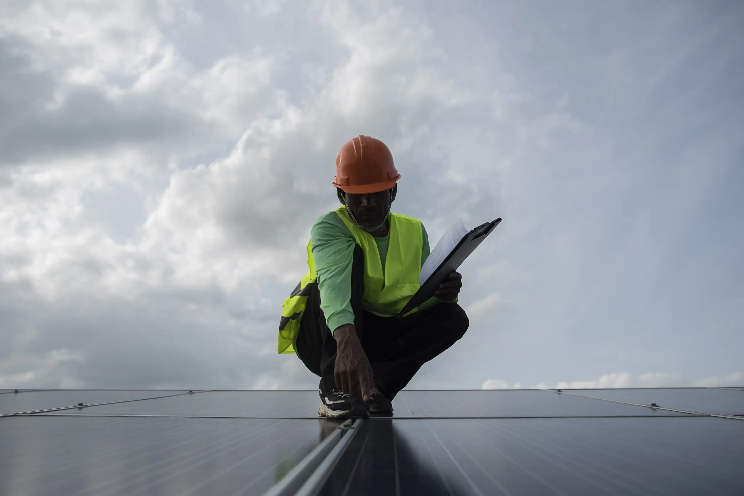 A professional wearing safety gear examines a solar panel on an elevated surface.