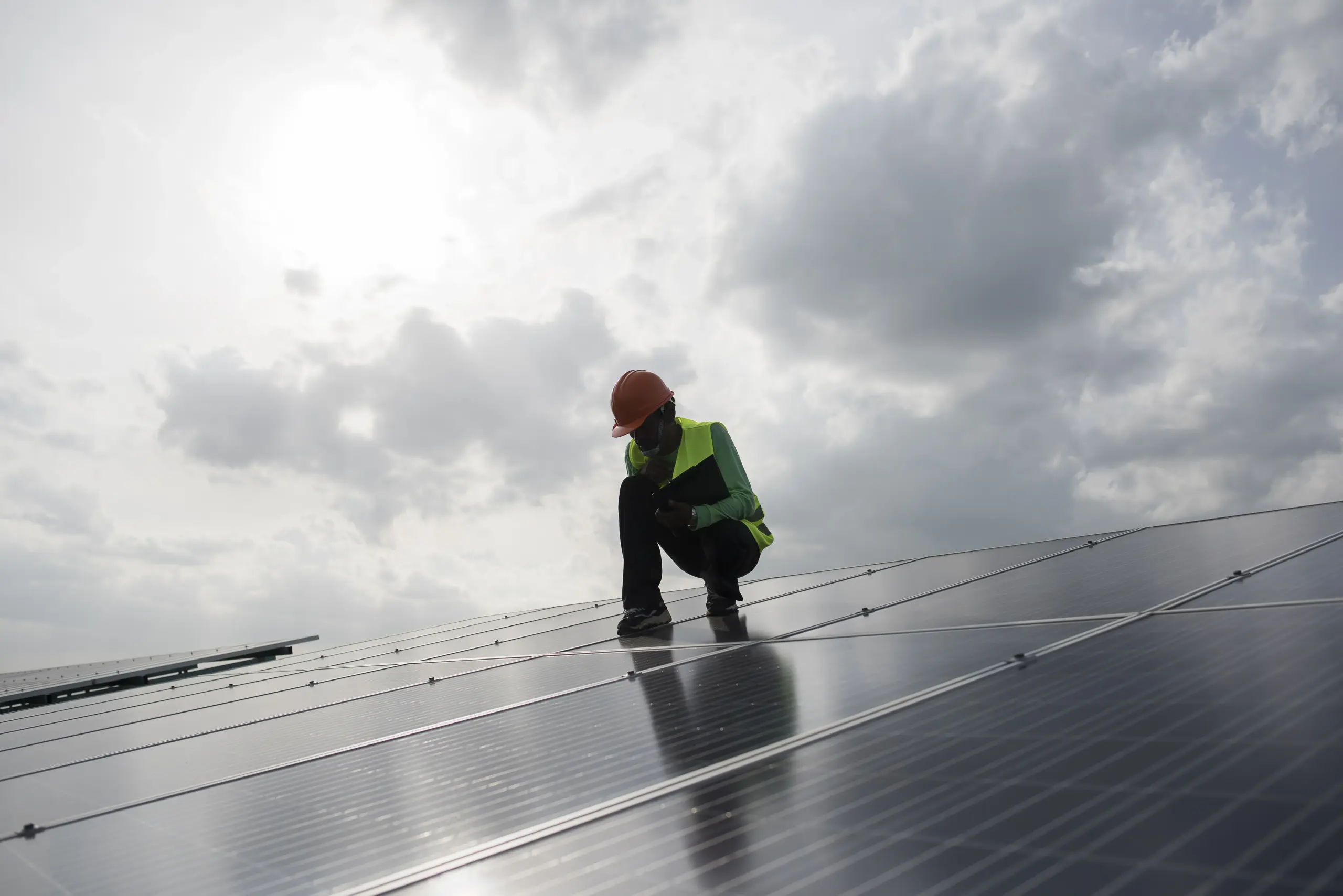 A solar energy professional in safety attire examines a panel at a height.